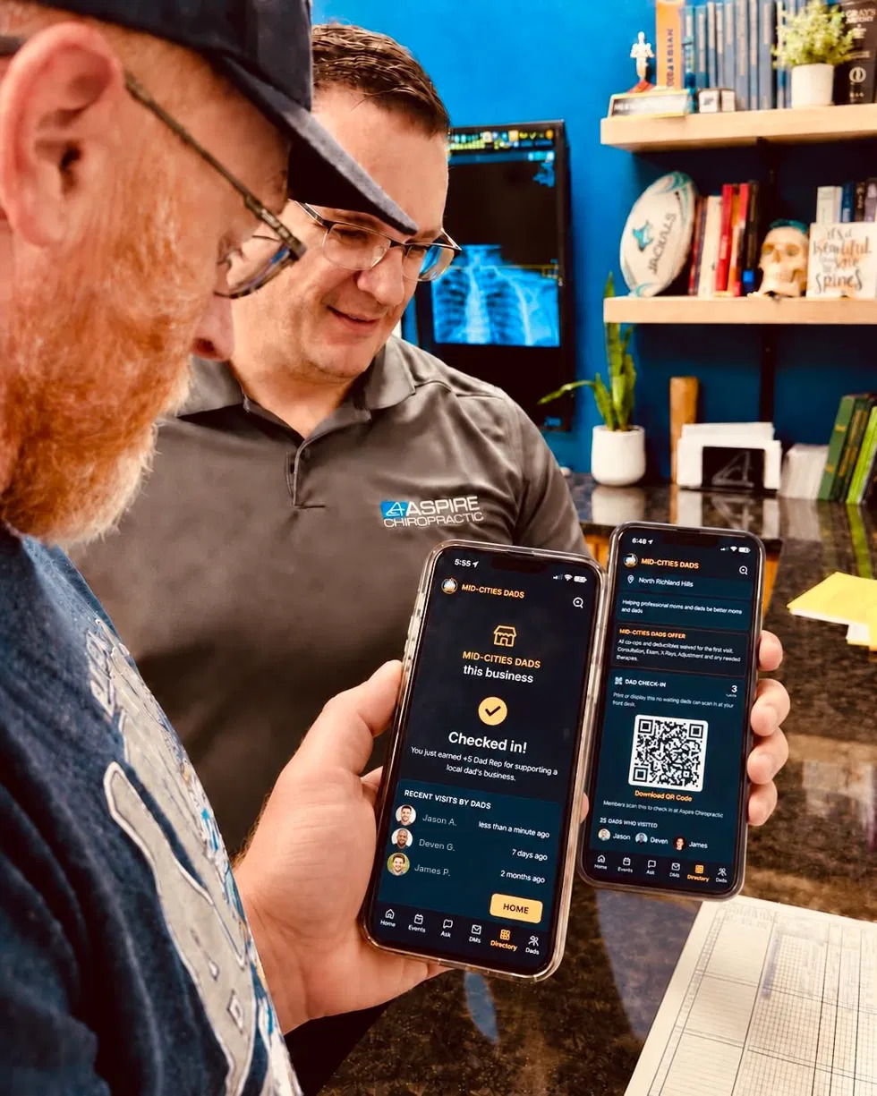 Two dads in an office showing the app's business check-in screens on their phones.