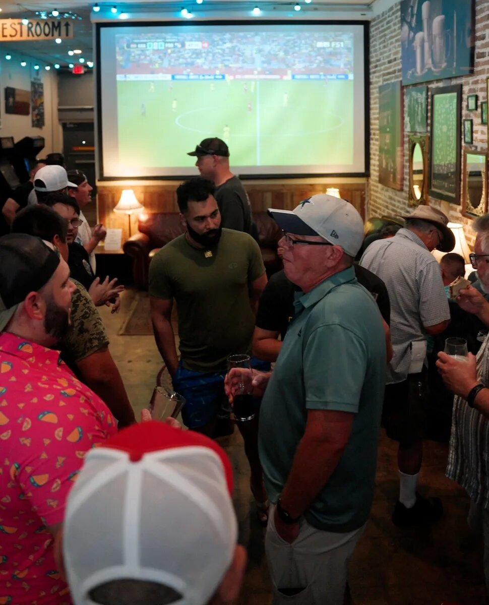 Dads talking together beneath the match screen at Turning Point Beer