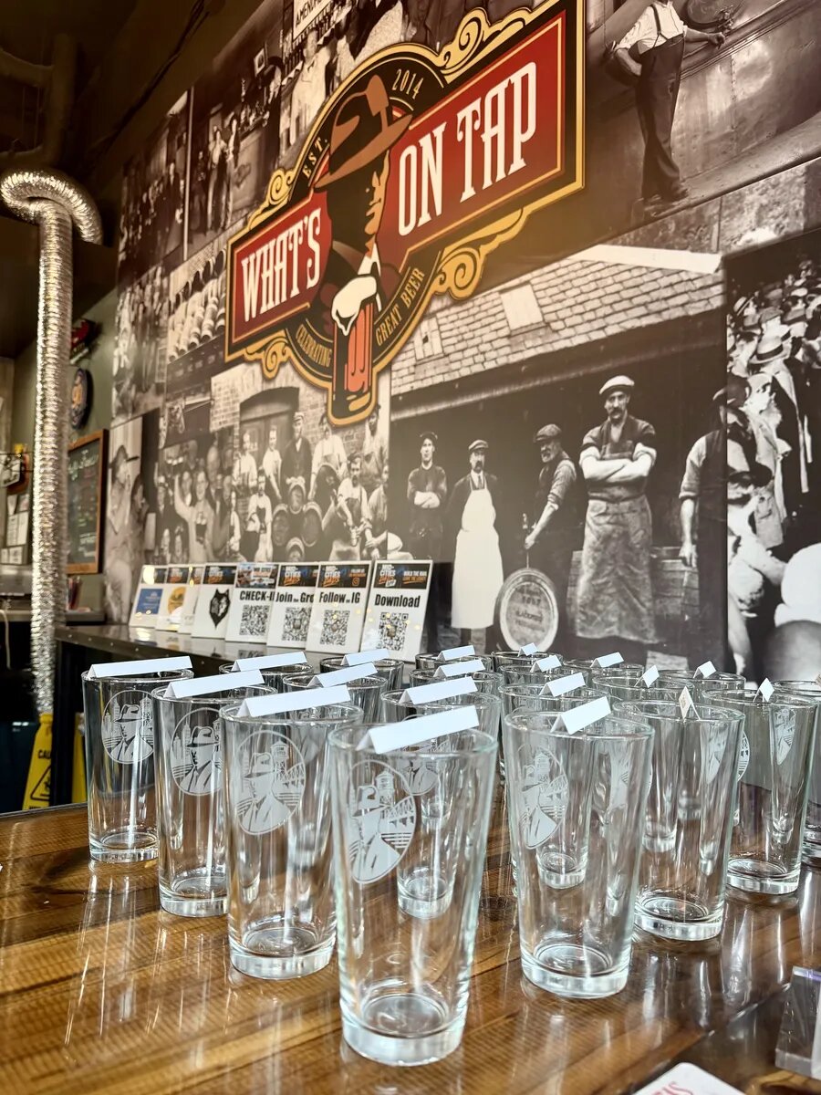 Collectible glasses lined up beside the check-in signs at What's On Tap